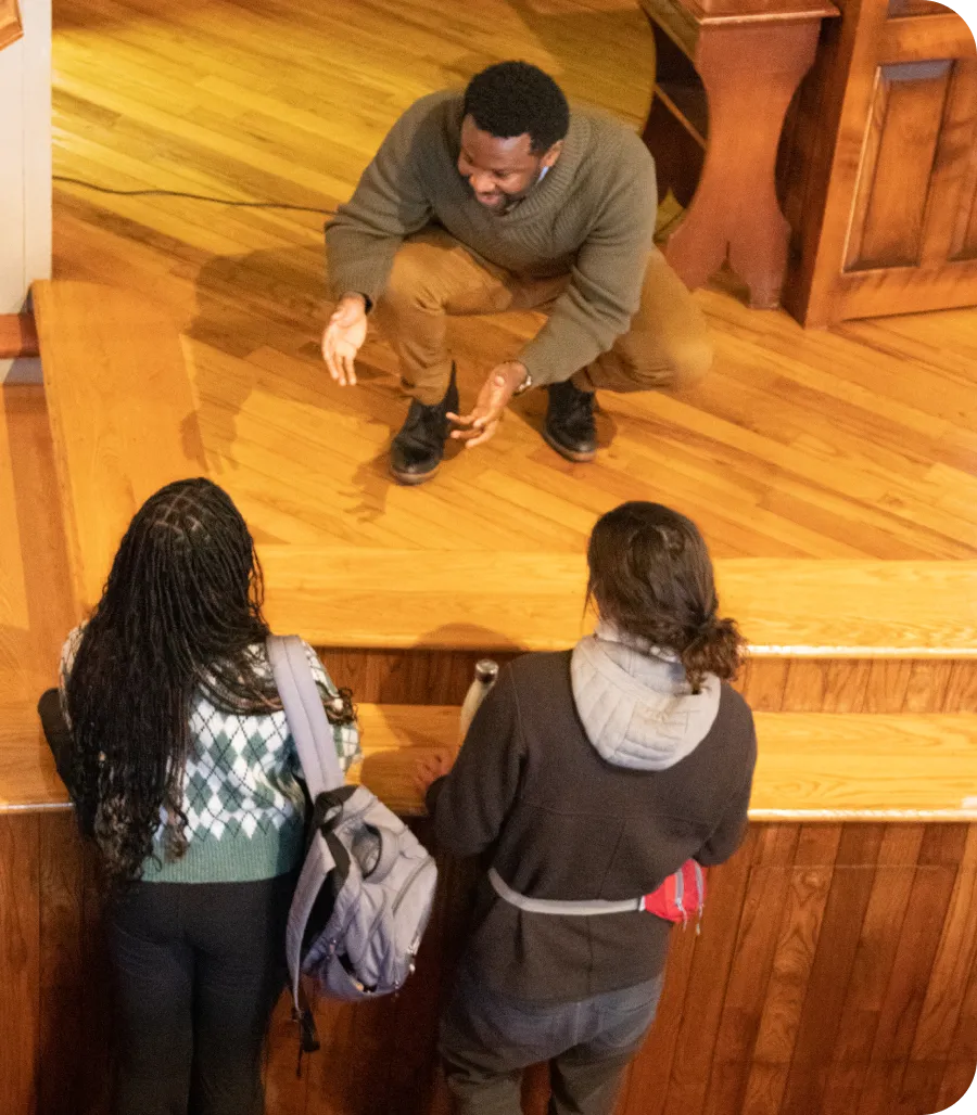 Deo Mwano kneeling to talk with two students